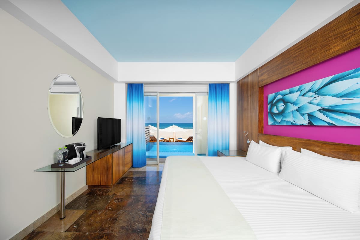 Ein Hotelzimmer mit Bett, Fernseher, Schreibtisch mit Kaffeemaschine und Blick auf den Strand.