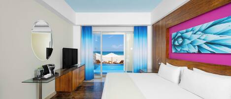 A hotel room with a bed, a TV, a desk with a coffee maker, and a view of the beach.
