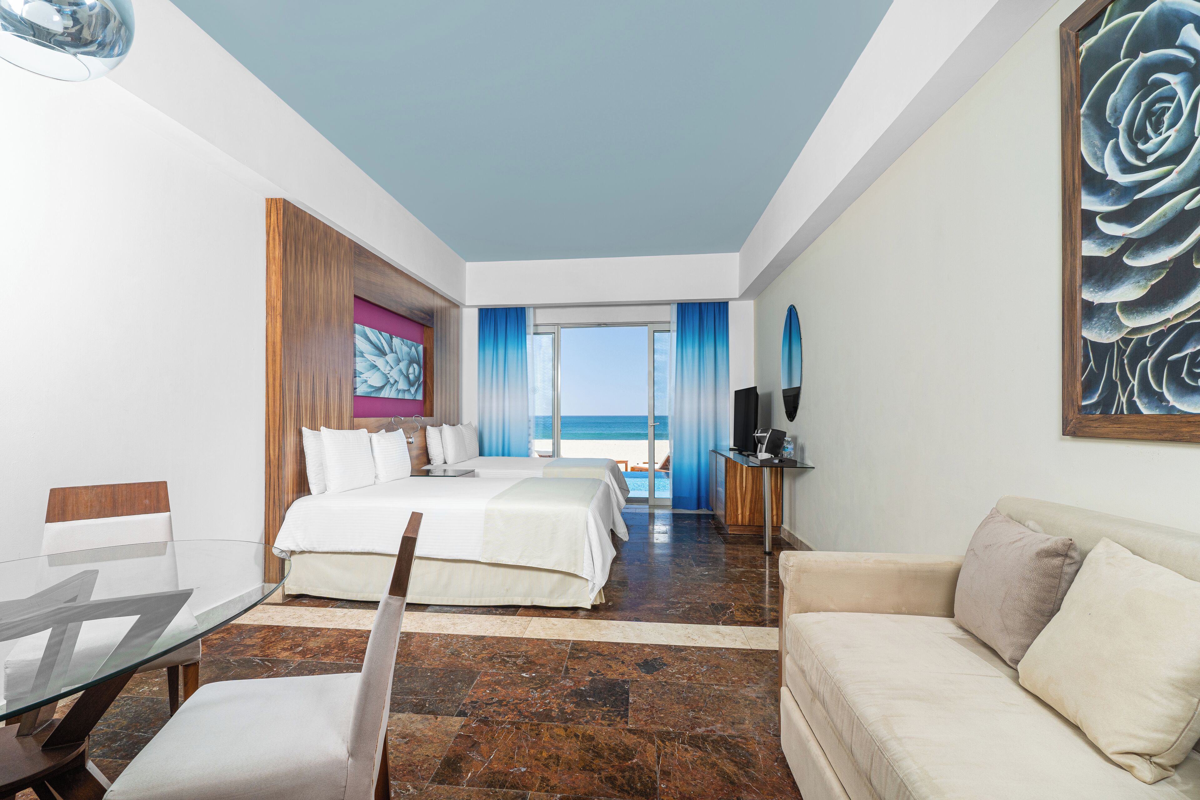 Quarto de hotel com cama, mesa de vidro, sofá e vista para o mar.