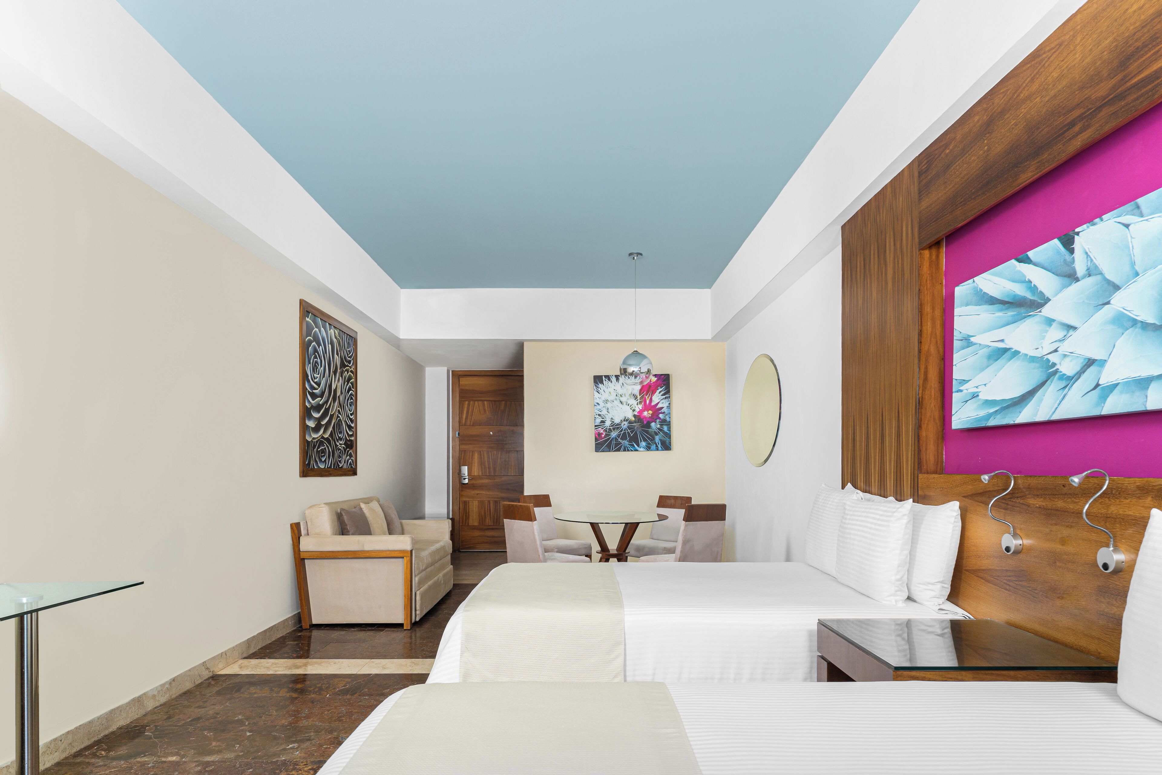 Una habitación de hotel con cama, escritorio, silla, mesa y obras de arte en las paredes.