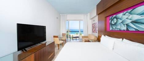 A hotel room with a large bed, a TV on a wooden cabinet, a painting on the wall, and a view of the sea through the window.