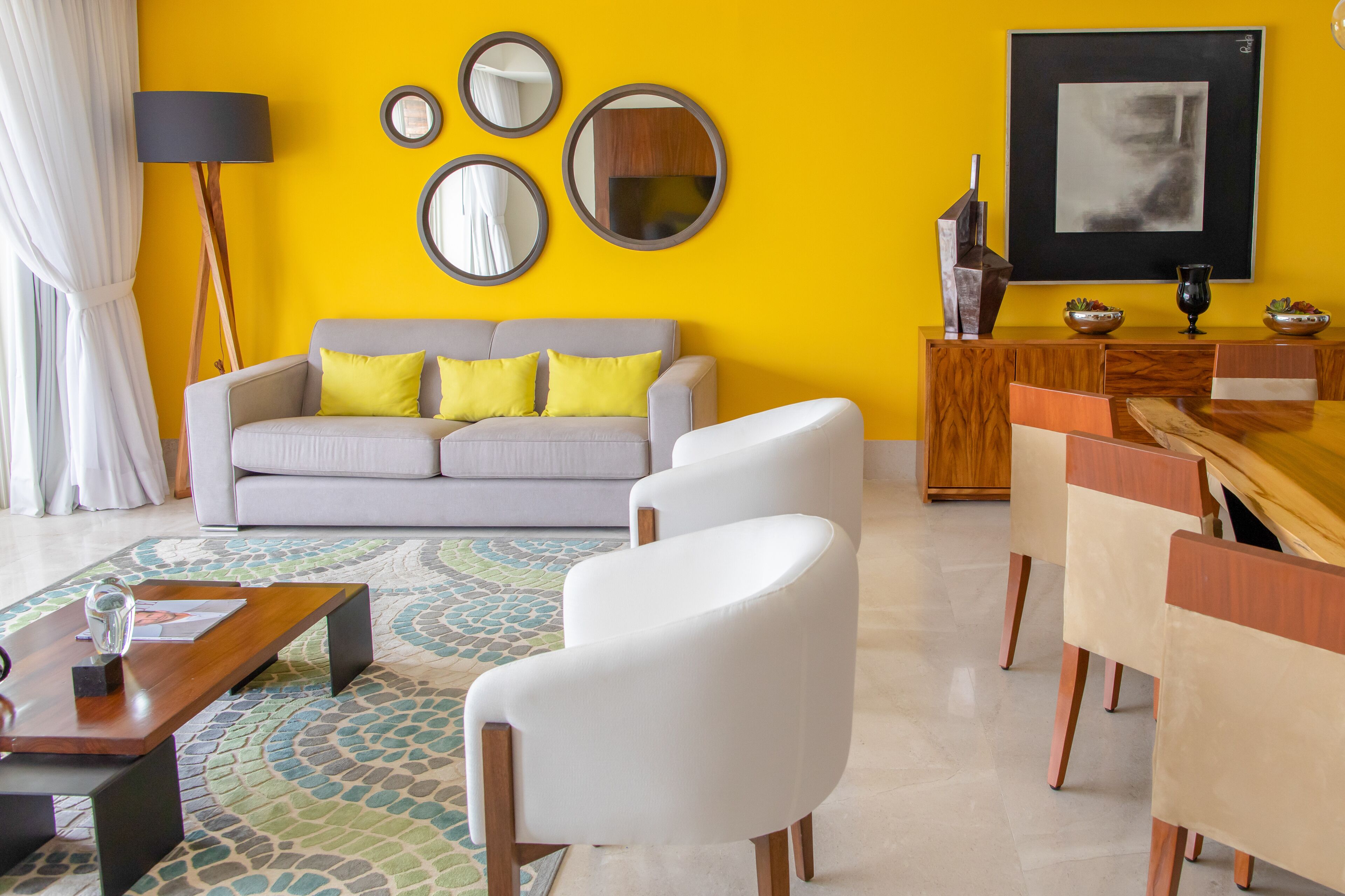 Ein Wohnzimmer mit einer Couch, zwei Sesseln, einem Couchtisch, einem Esstisch mit Stühlen, einer Lampe und einem Bild an der Wand.