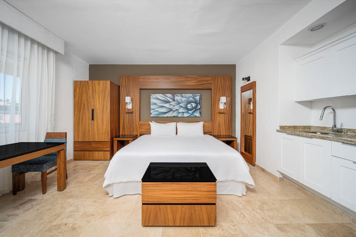 Ein Hotelzimmer mit einem großen Bett, einem Holzschrank, einem Schreibtisch und einer Küchenzeile.