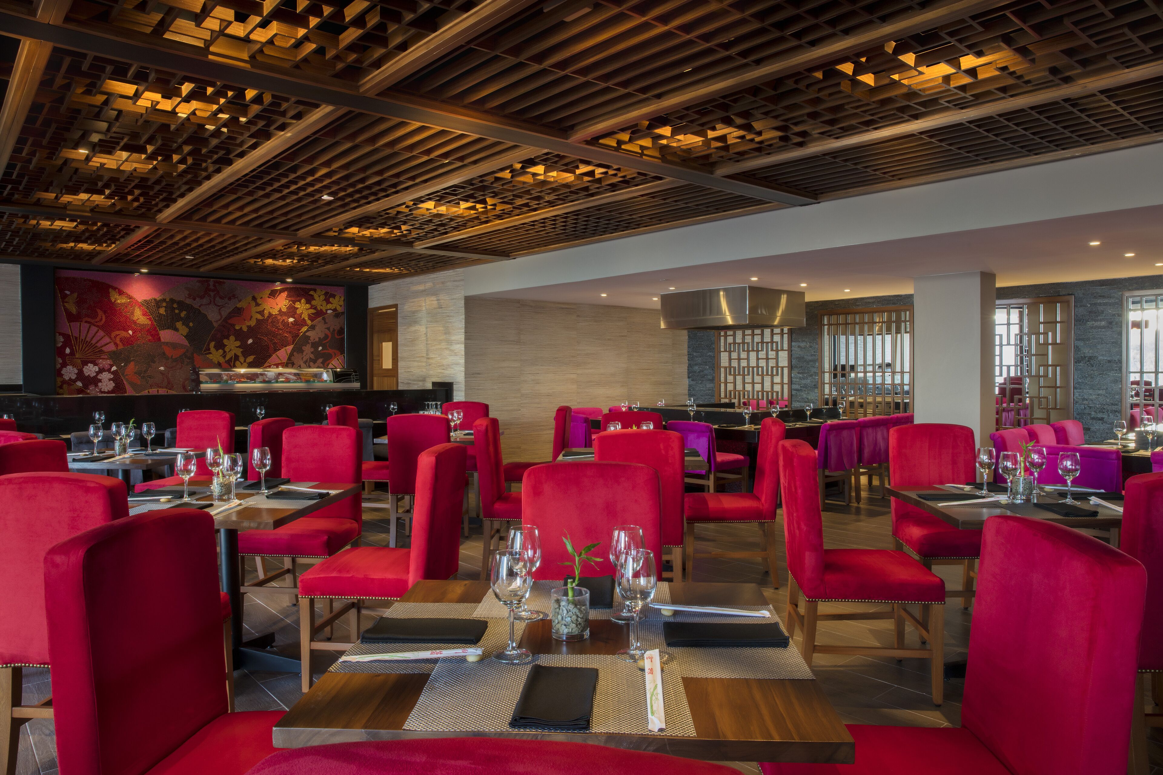 A restaurant with red upholstered chairs, wooden tables, and a decorative ceiling.
