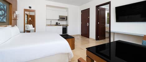 A hotel room with a large bed, a TV, a desk, and a kitchenette.