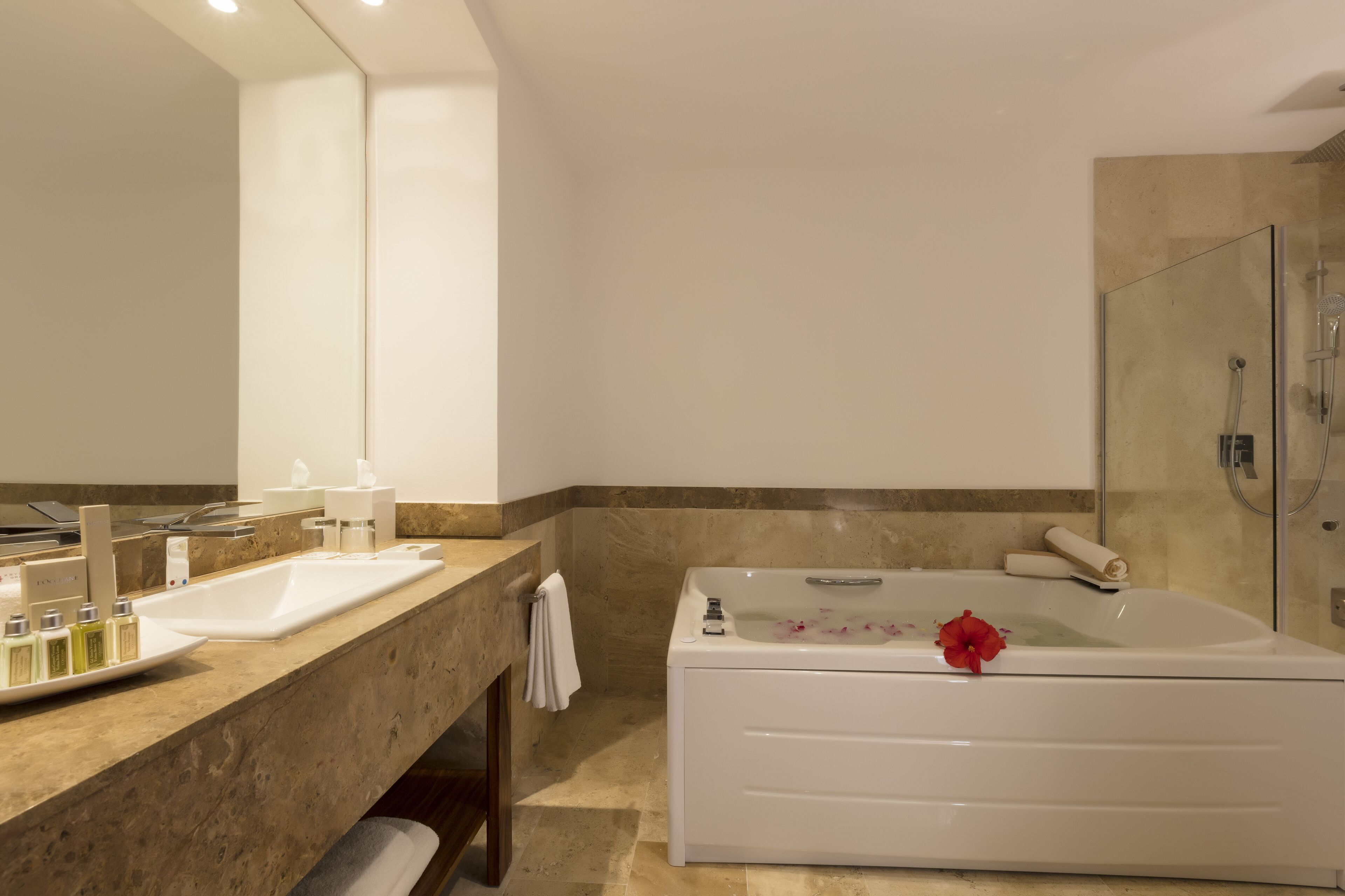 A modern bathroom with a large white bathtub, a separate shower area, and a marble countertop with toiletries.