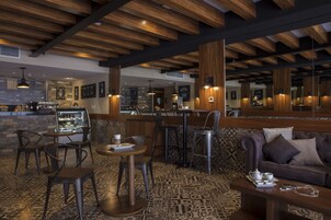 A cozy cafe with wooden ceiling beams, patterned carpet, and a mix of bar stools and tables.