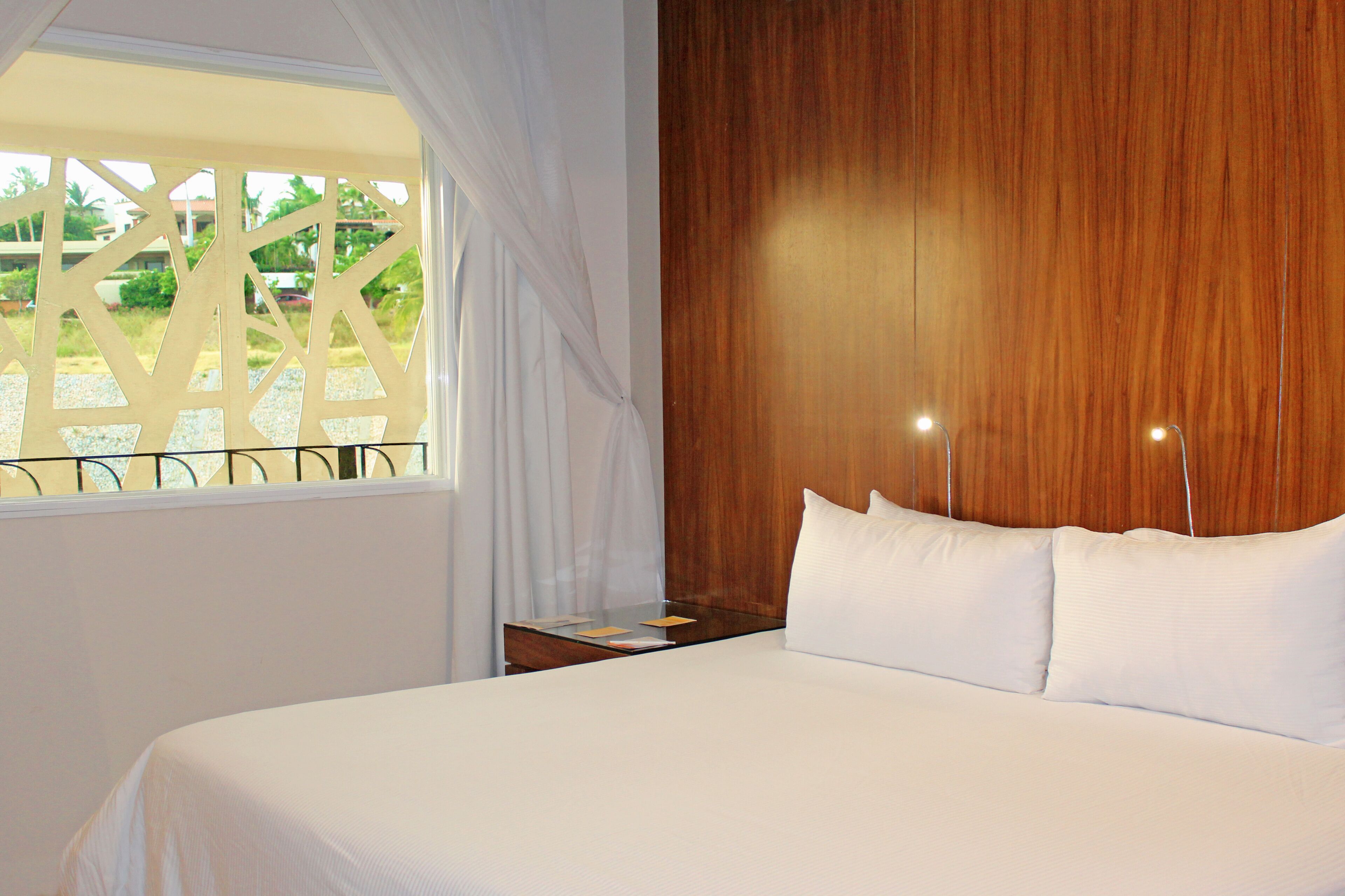 A hotel room with a large bed, wooden headboard, and a window with curtains.