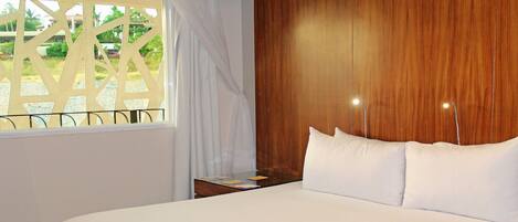 A hotel room with a large bed, wooden headboard, and a window with curtains.