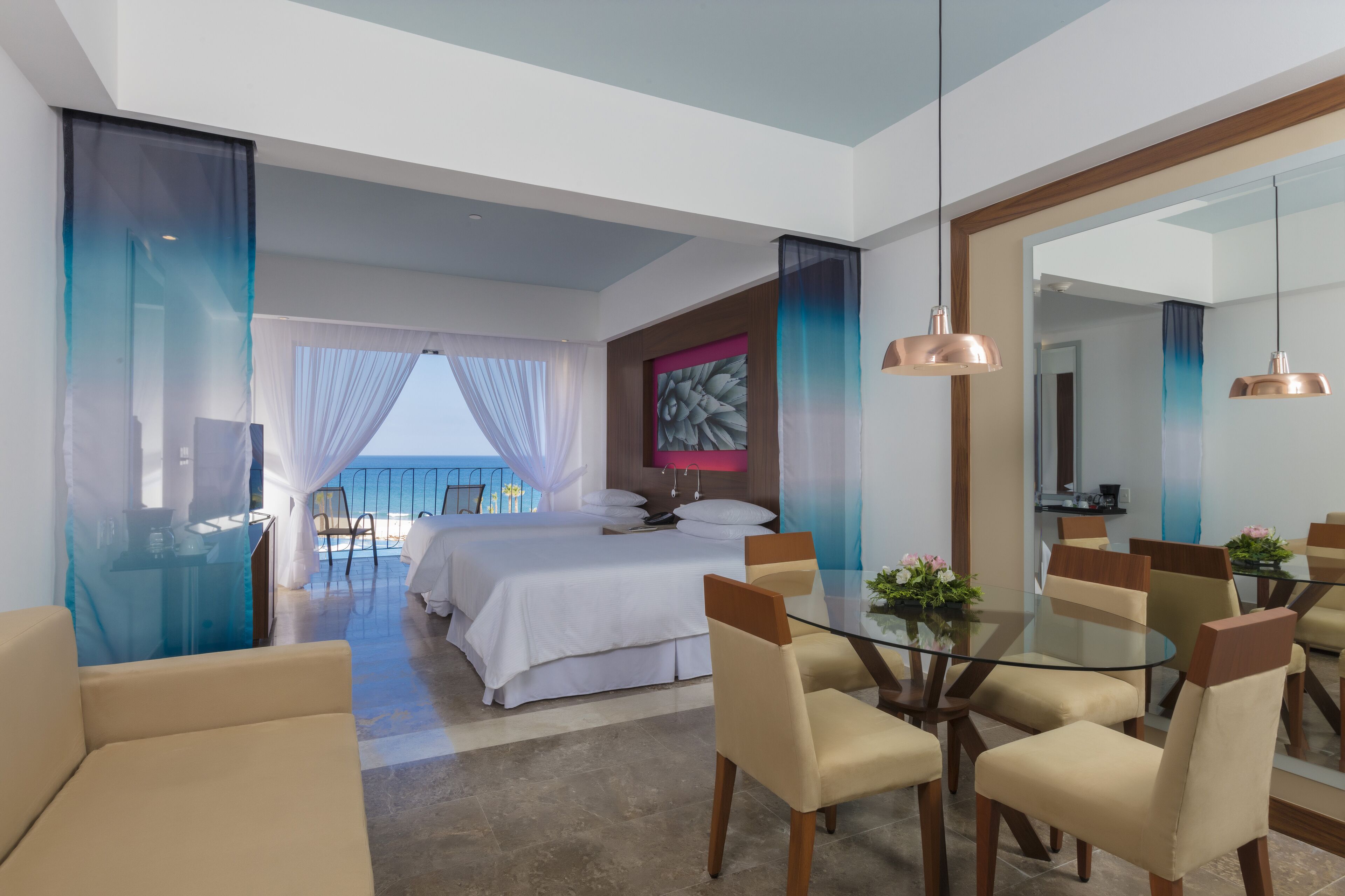Una habitación de hotel moderna con balcón, zona de comedor con mesa de vidrio y un espejo grande.