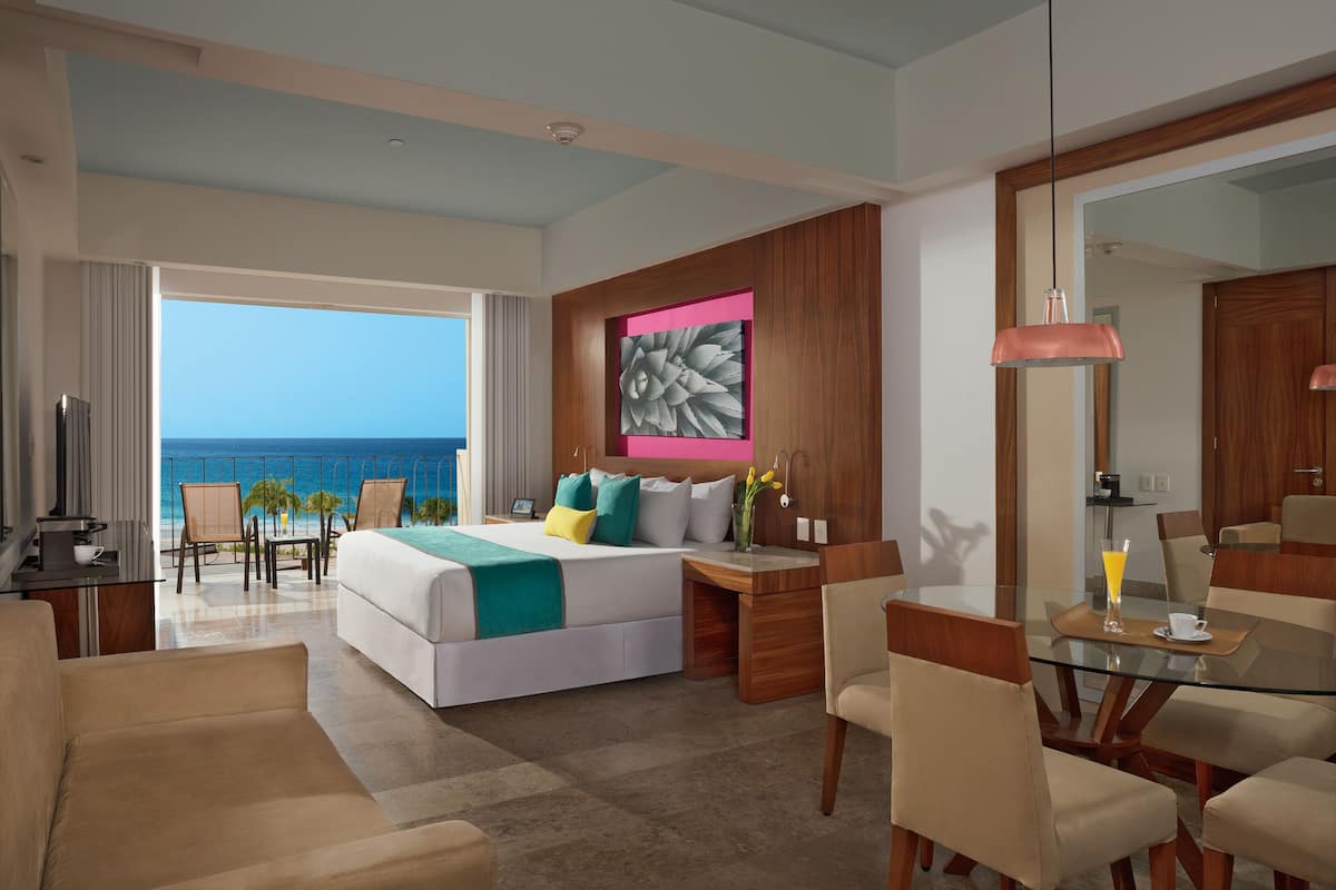 Ein modernes Hotelzimmer mit einem großen Bett, einem Balkon mit Meerblick, einem Essbereich mit Glastisch und einer Wand mit Holzvertäfelung.