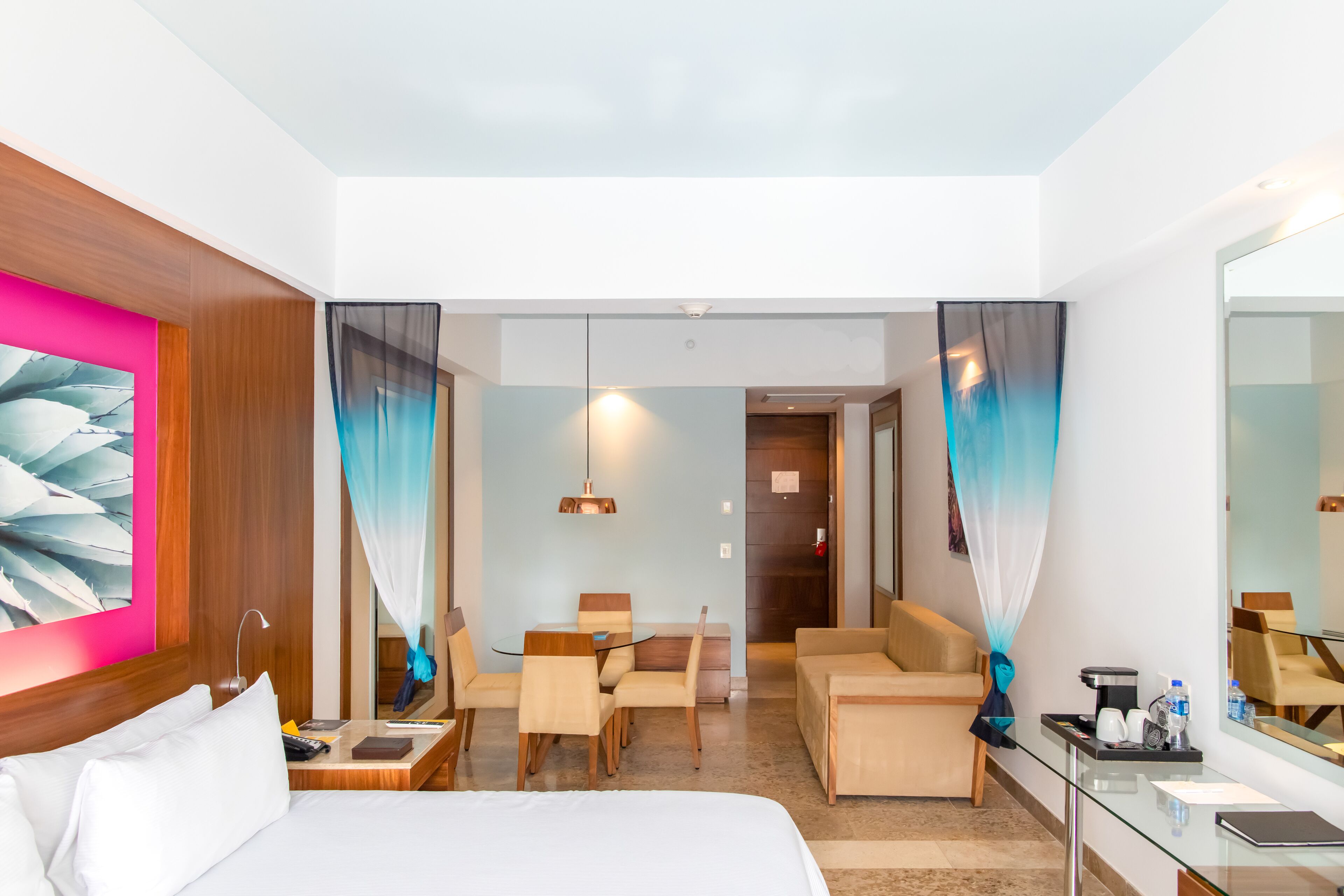 Une chambre d’hôtel comprenant un lit, un bureau, une chaise, un canapé, une cloison en verre et un grand miroir.