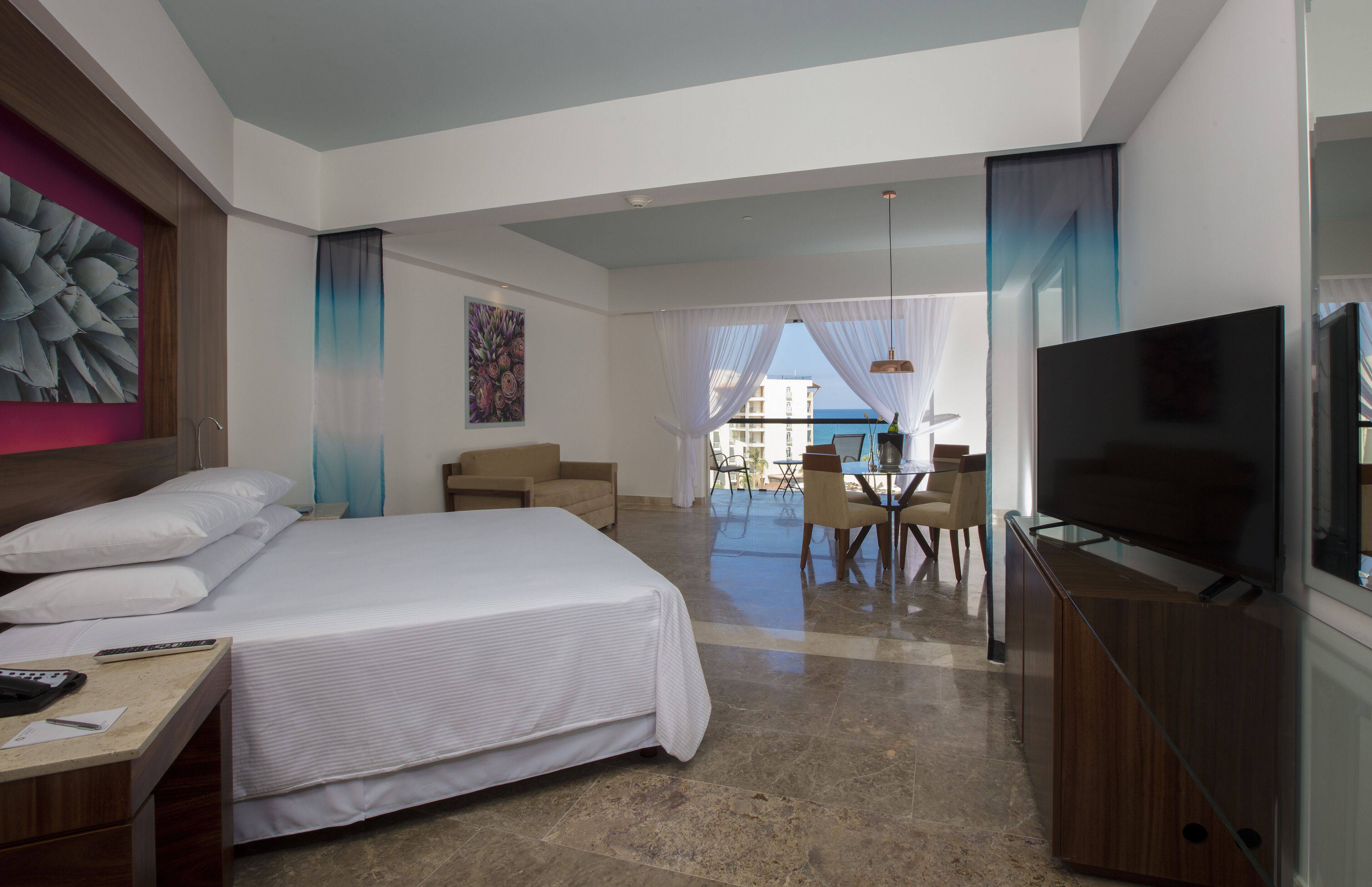 A hotel room with a large bed, a TV, a desk, and a balcony with a view.