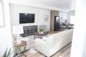 Una sala de estar moderna con un sofá blanco, una mesa de centro y un televisor montado en la pared.