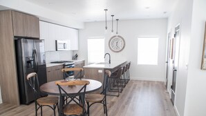 A modern kitchen with a central island, stainless steel appliances, and a wooden dining table with chairs.
