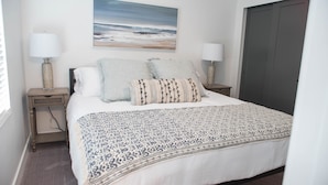 A neatly arranged bedroom with a large bed, two bedside tables with lamps, a wall-mounted painting, and a closed door.