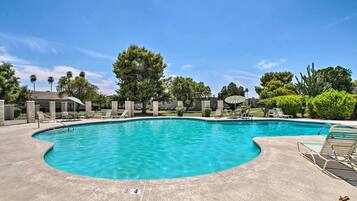A swimming pool with a curved edge, surrounded by lounge chairs and a covered area.