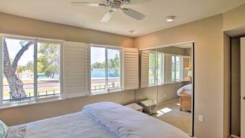 Un dormitorio con cama, ventilador de techo, ventana grande con contraventanas y vista a una piscina.