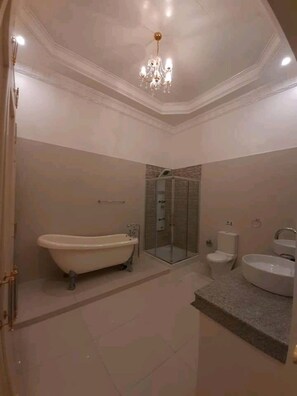 A spacious bathroom with a freestanding bathtub, a glass-enclosed shower, a toilet, and a sink. - Canoy's Mansion Apartelle in Dalaguete Cebu (Dalaguete)