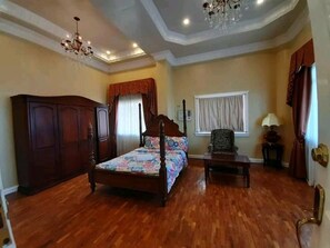 A bedroom with a wooden bed, a nightstand, a chair, a wardrobe, and a chandelier. - Canoy's Mansion Apartelle in Dalaguete Cebu (Dalaguete)