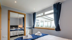 A hotel room with a large bed, a mirror, a window with curtains, and a view of the sea.