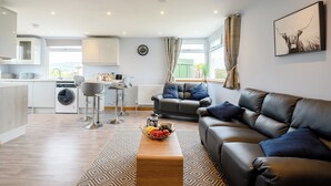 A modern living room with a leather sofa, a coffee table with fruit, and a kitchen in the background.