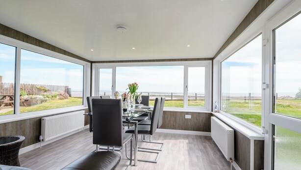 A modern dining area with a view of the sea, featuring a table set for two, a sofa, and a wicker chair.