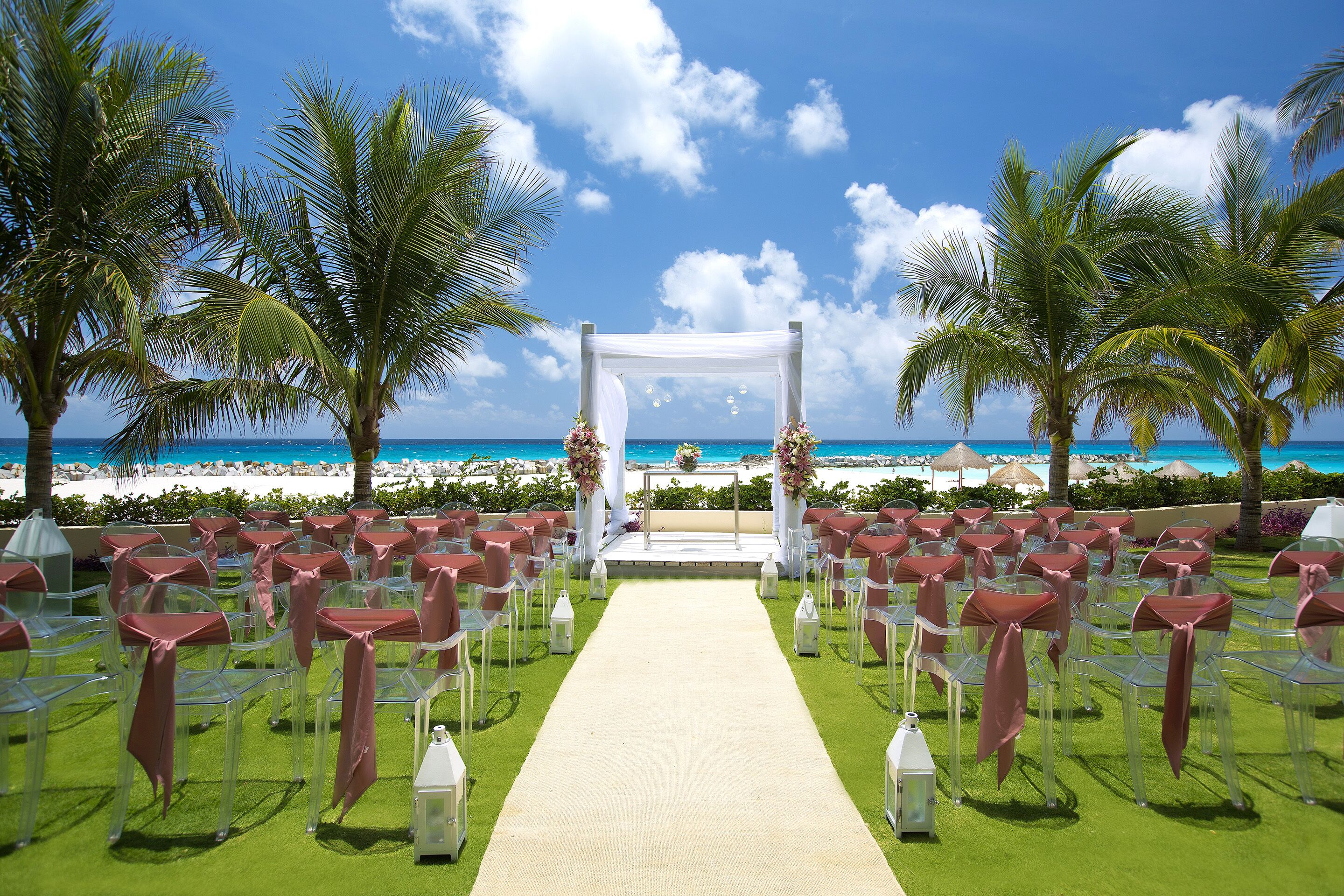 Decoración para una boda en la playa, con un pasillo blanco, sillas transparentes y vista al océano.