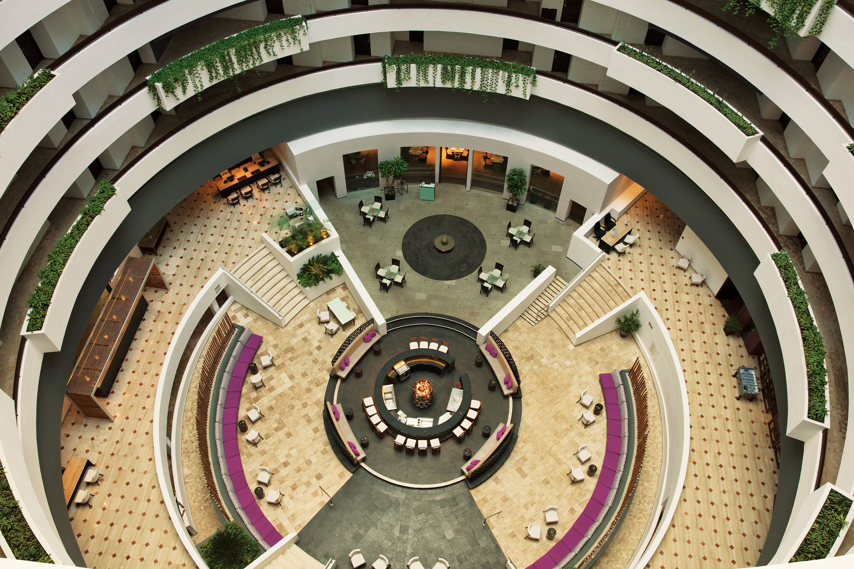 A multi-level atrium with circular seating areas, a central fountain, and greenery.
