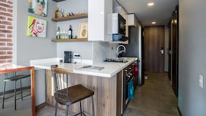 A compact kitchen with a white countertop, wooden bar stools, and a microwave. - Loslan Real Estate (Medellín)