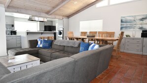 A spacious living area with a sectional sofa, a dining table, and a kitchen in the background.