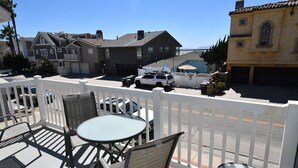 A balcony with outdoor seating, a white pick-up truck, and residential buildings in the background.