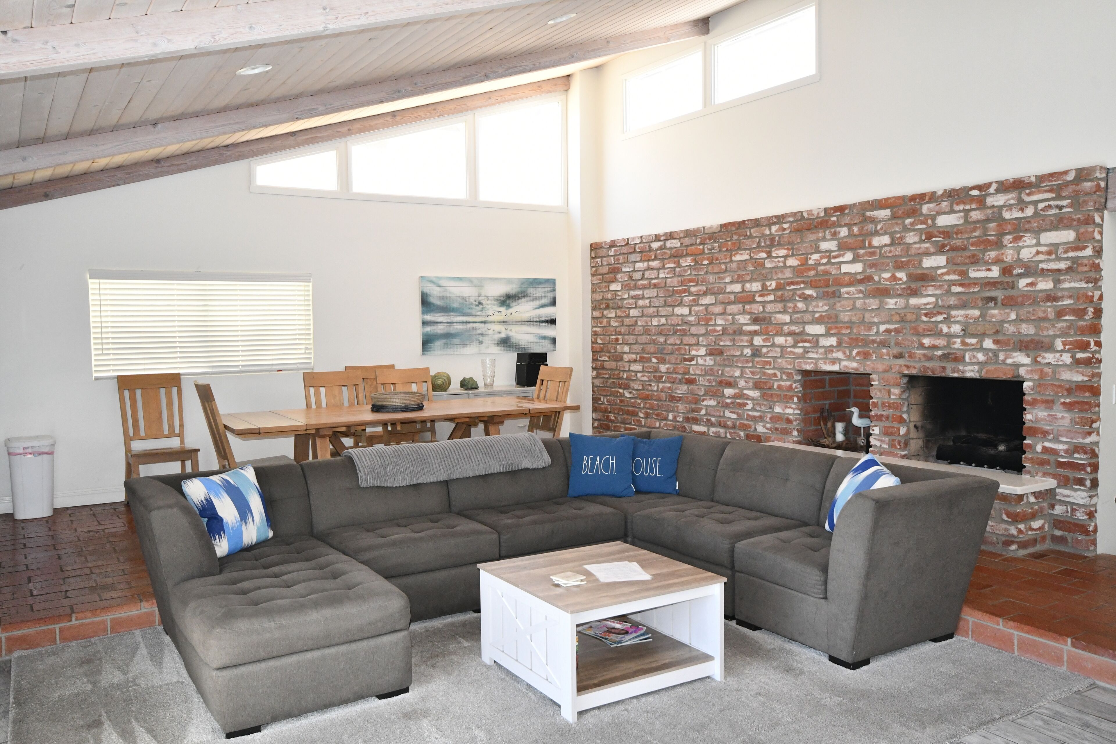 A modern living room with a sectional sofa, a coffee table, a brick fireplace, and a dining area with a wooden table and chairs.