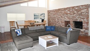 A modern living room with a sectional sofa, a coffee table, a brick fireplace, and a dining area with a wooden table and chairs.