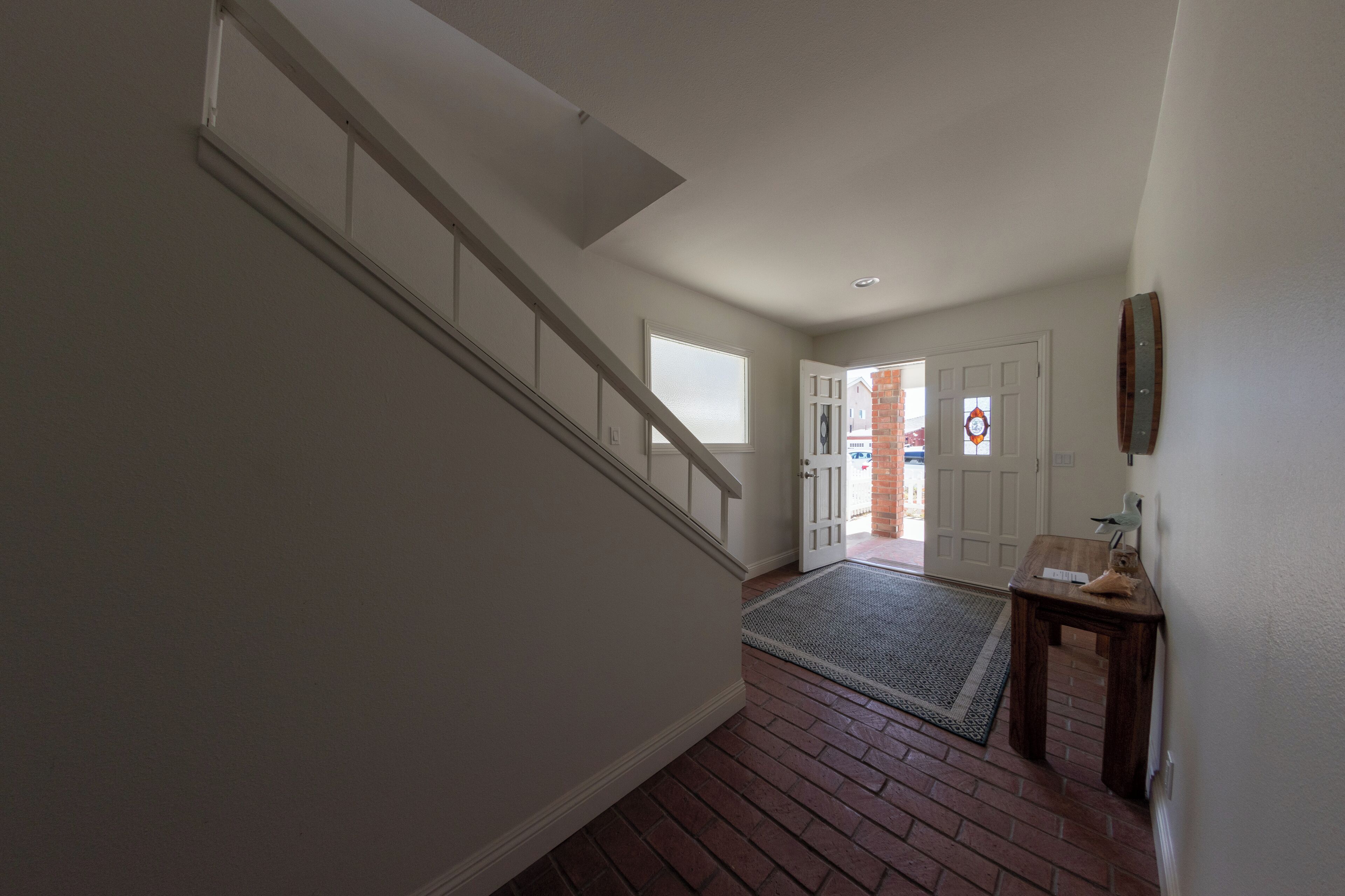 A hallway with a wooden staircase, a doormat, and a door leading to another room.