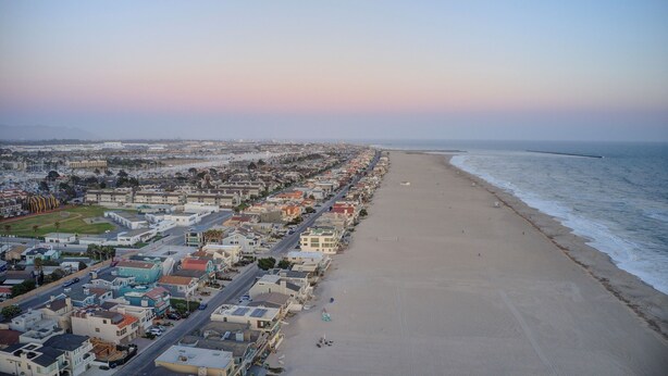 A coastal cityscape with a wide beach, residential buildings, and a clear sky.