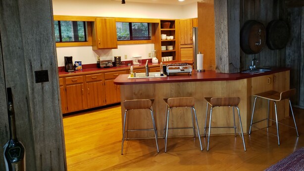 A modern kitchen with wooden cabinets, a central island with bar stools, and a ceiling fan. - Awesome Lake House with Natural Beach, Huge Dock, and Sunset Views. Sleeps 9 (Moneta)
