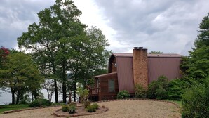 A cabin with a gravel driveway, surrounded by trees and a lake. - Awesome Lake House with Natural Beach, Huge Dock, and Sunset Views. Sleeps 9 (Moneta)