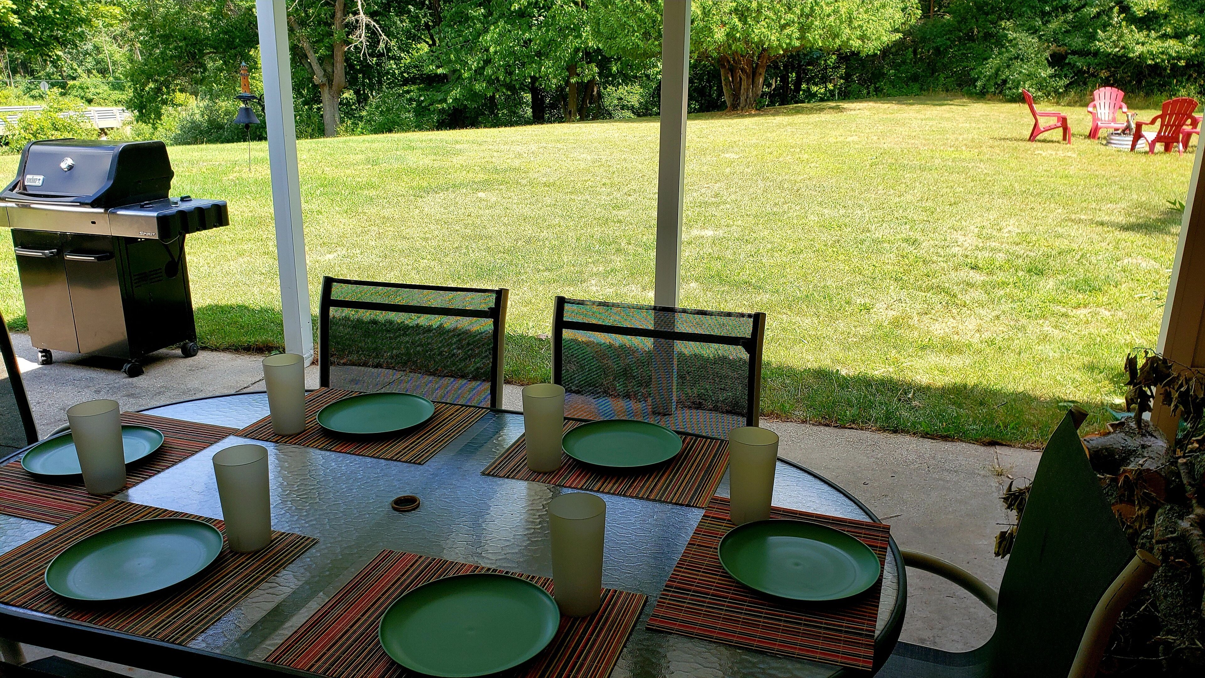 Une terrasse extérieure avec une table dressée pour quatre personnes, entourée de chaises, et un barbecue à l’arrière-plan.