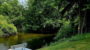 Eine Holzterrasse an einem ruhigen Fluss mit einer Bank und einem gelben Schild.