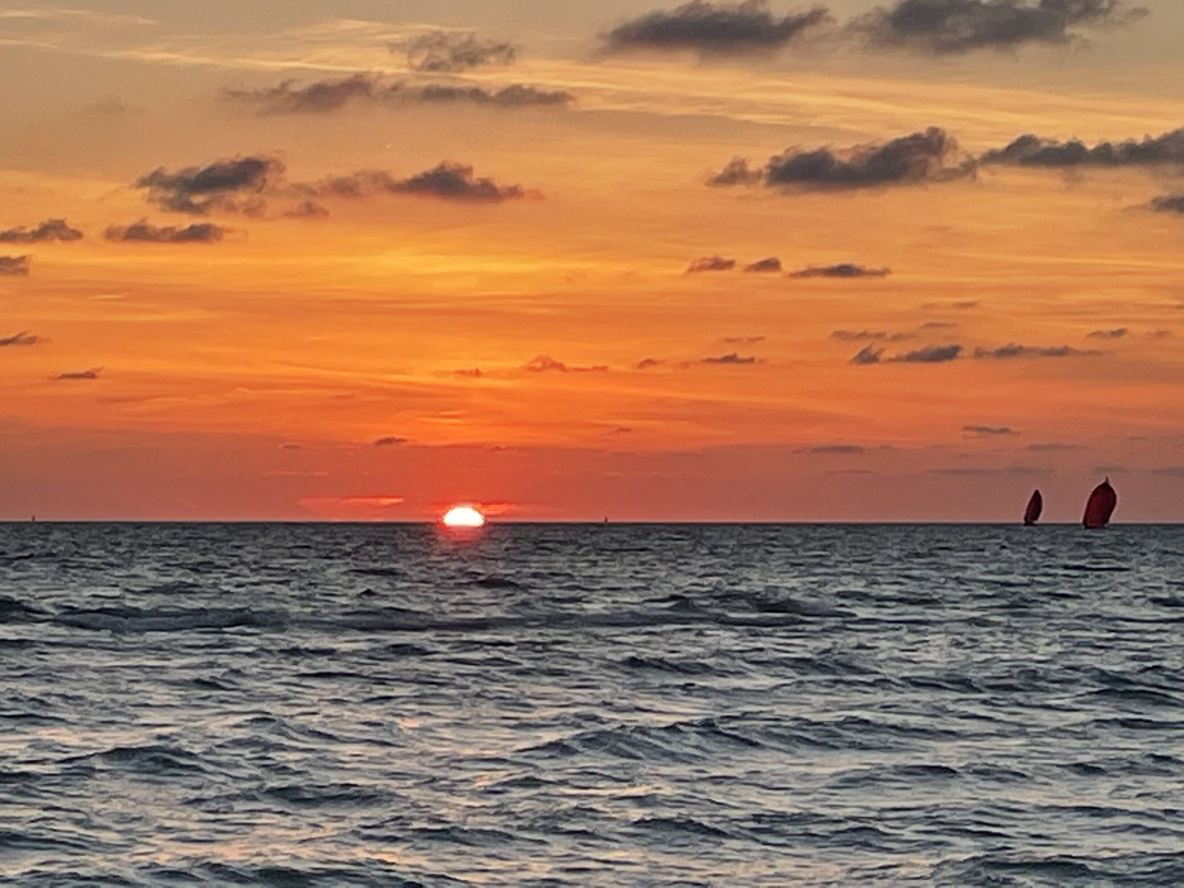 Een zonsondergang boven de zee met twee zeilboten.