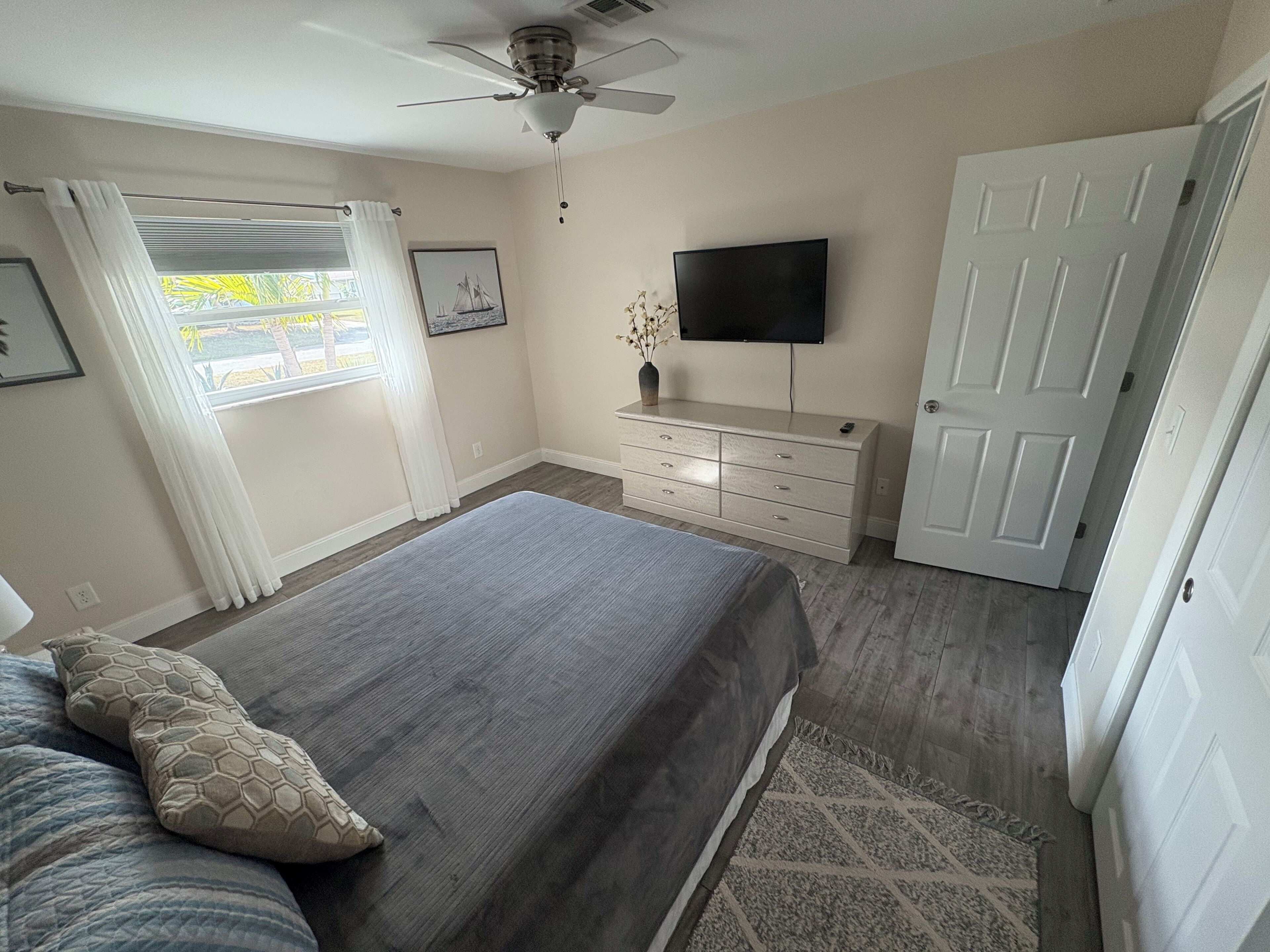 A bedroom with a bed, a dresser, a television, and a door.