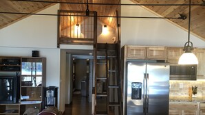 Un vaste espace de vie de style loft, doté d’un plafond en bois, d’un lit en mezzanine, d’une cuisine équipée d’appareils modernes et d’un coin repas avec un comptoir en granit.