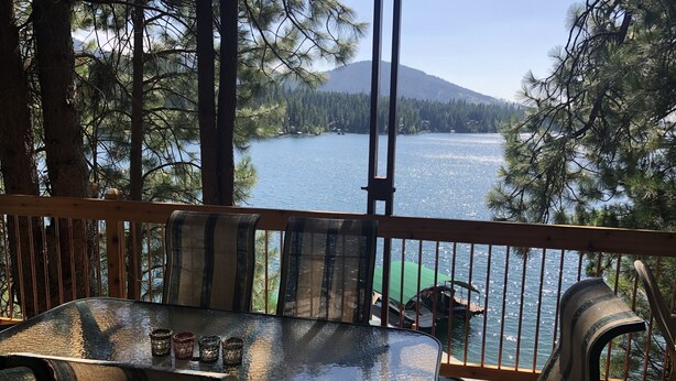 Une terrasse en bois avec une table et des chaises en verre, donnant sur un lac.