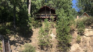 Un chalet au bord du lac, doté d’une terrasse en bois et entouré d’une forêt dense de pins.
