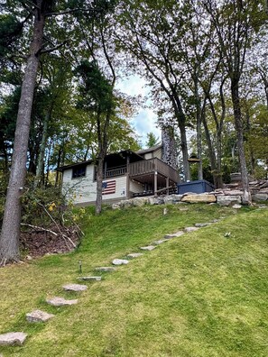 A rustic cabin with a stone staircase leading to a wooden deck, surrounded by trees and a grassy area.