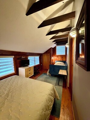 A bedroom with a bed, a desk, a chair, and a television.