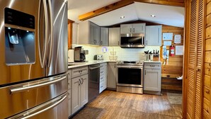 A modern kitchen with stainless steel appliances, wooden flooring, and a high ceiling with exposed beams. - Lakefront Cabin w/ Hot Tub, Views & Fireplace (Lake Harmony)