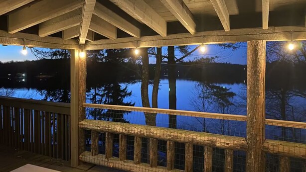 A wooden deck with a view of a lake at dusk. - Lakefront Cabin w/ Hot Tub, Views & Fireplace (Lake Harmony)