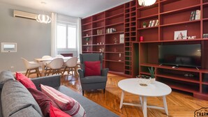 En moderne stue med en grå sofa, en rød og grå lænestol, et hvidt sofabord og en rød reol.